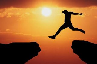 Silhouette of a person jumping across a cliff during sunset, representing a leap of faith